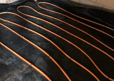 Coiled orange underfloor heating pipes clipped to dpm