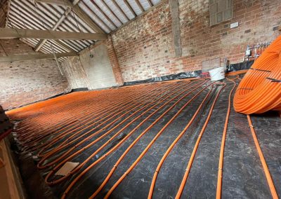 Underfloor heating project in a brick barn conversion : coiled orange pipes clipped to dpm and manifold